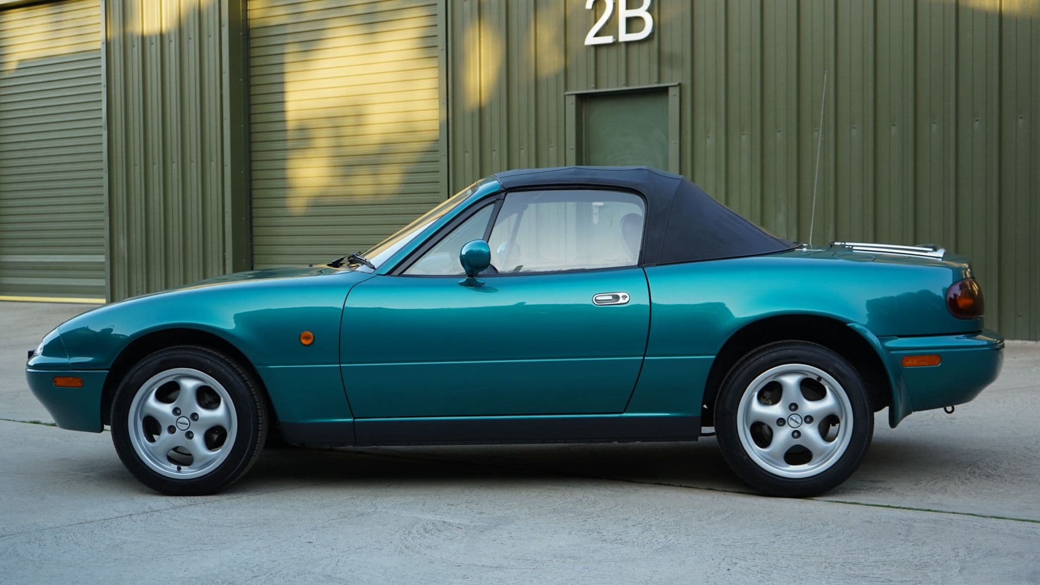 Green 1998 Mazda MX-5 Berkeley Edition in a side profile with the soft top raised, alternate composition.