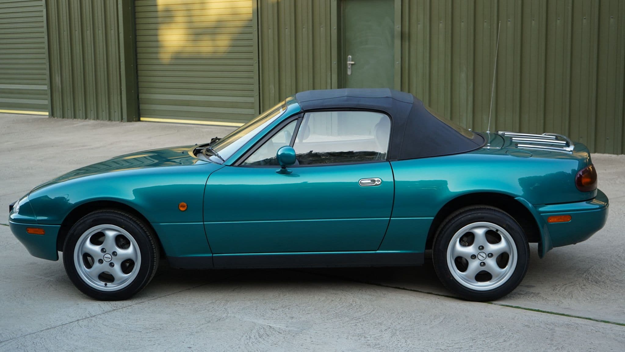 Green 1998 Mazda MX-5 Berkeley Edition in a side profile with the soft top raised.