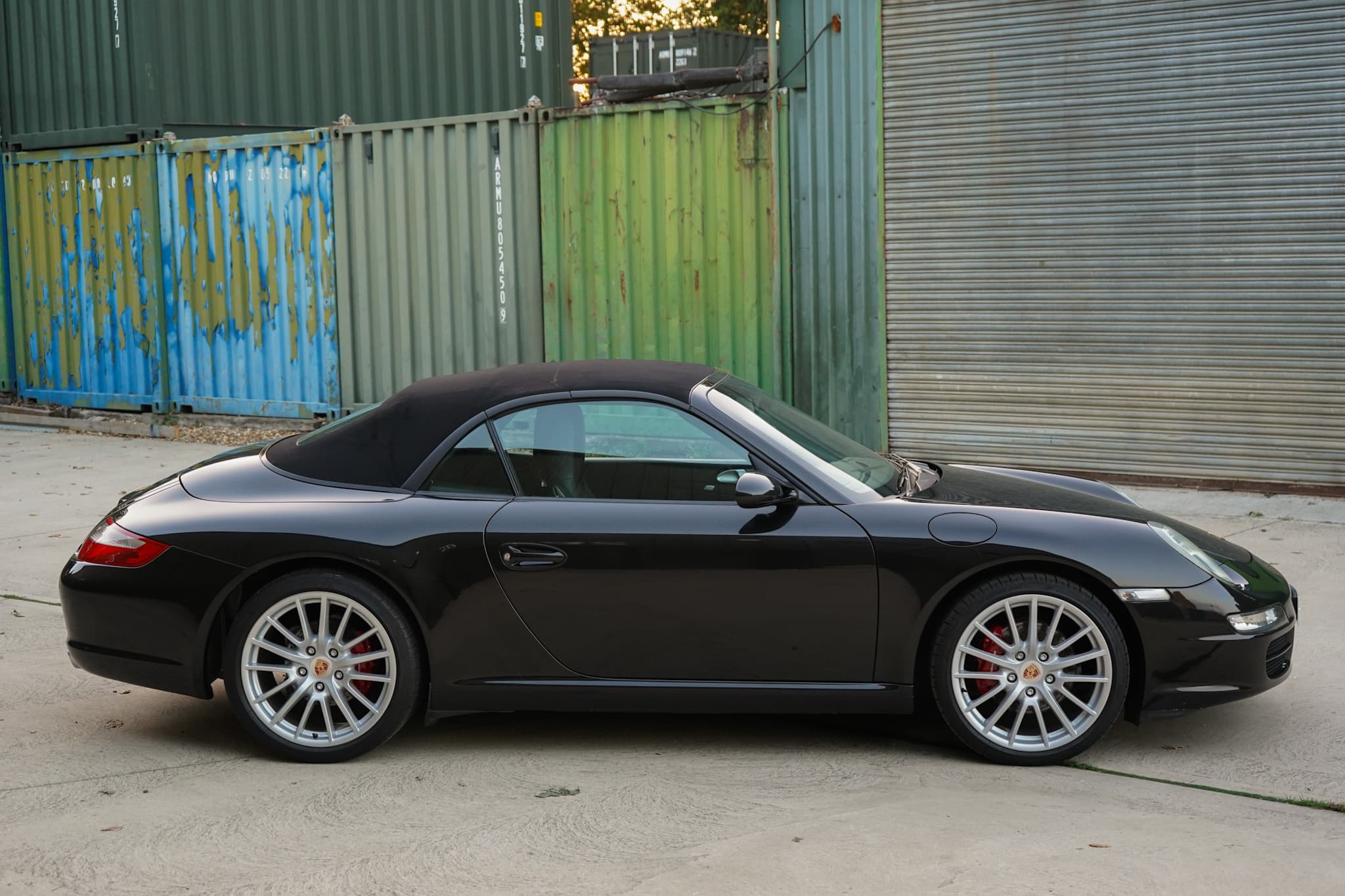 Black 2006 Porsche 911 (997) Carrera Cabriolet in a side profile with the soft top raised.