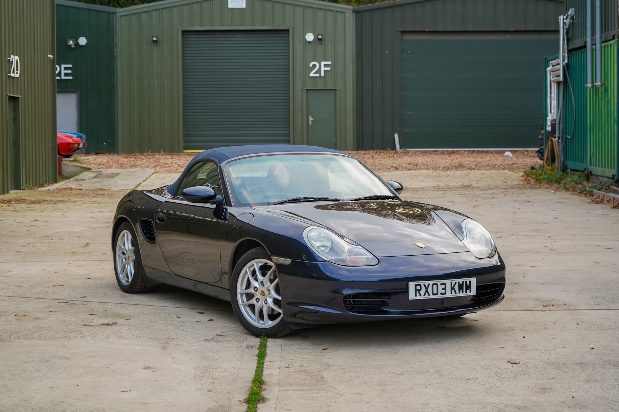 Dark blue 2003 Porsche Boxster (986) in a front three-quarter roof down.