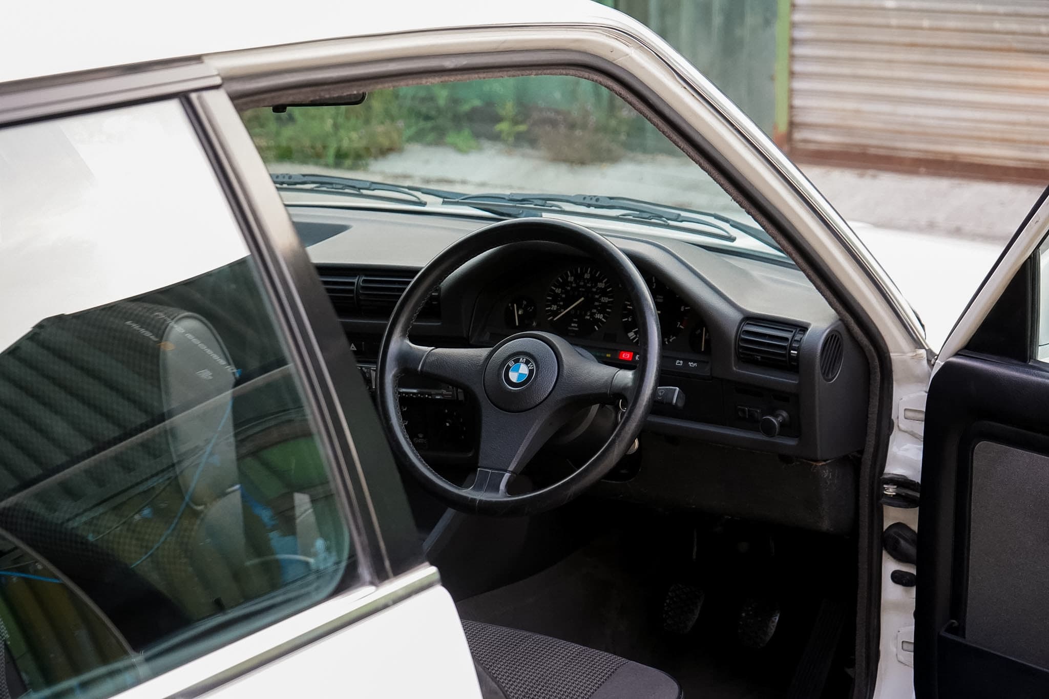 BMW 325i (E30) Manual Coupe steering wheel and dashboard through the open driver door.